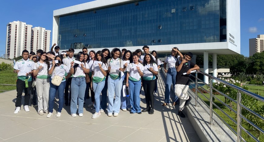 Na foto, há um grupo de estudantes posicionado em área externa em frente ao TRE-CE. As pessoas e...