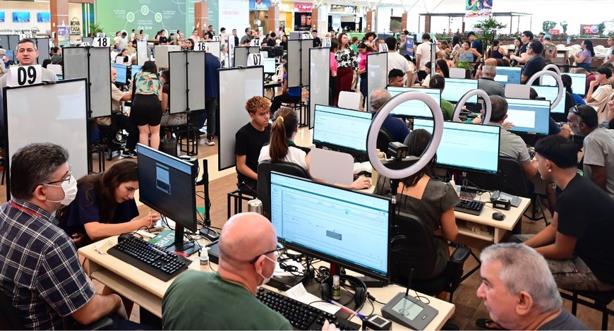 Na imagem, há diversas estações numeradas, cada uma com atendentes e pessoas sendo atendidas. As...