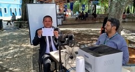 Na imagem, o presidente do TRE-CE está sentado, mostrando o título de eleitor para o registro. A...