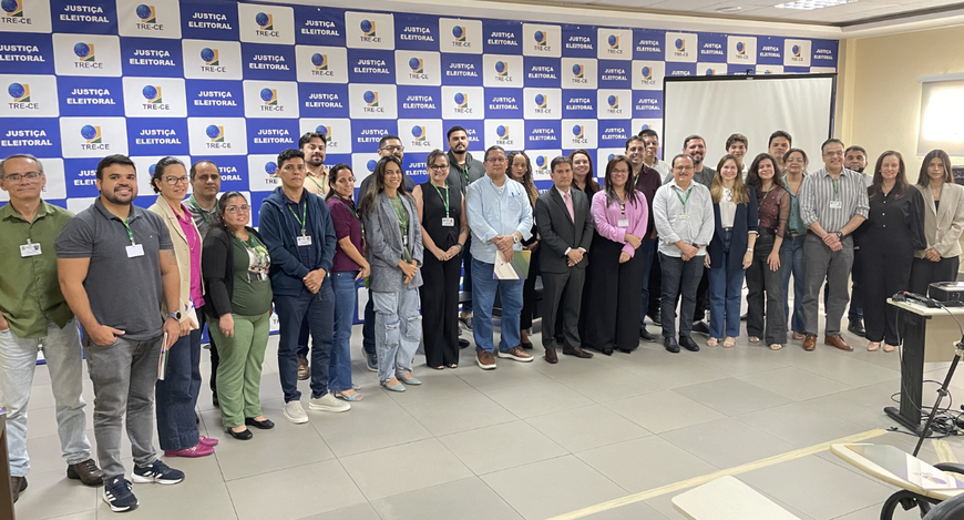 A imagem mostra um grupo de pessoas, entre homens e mulheres, posando lado a lado para a foto. A...