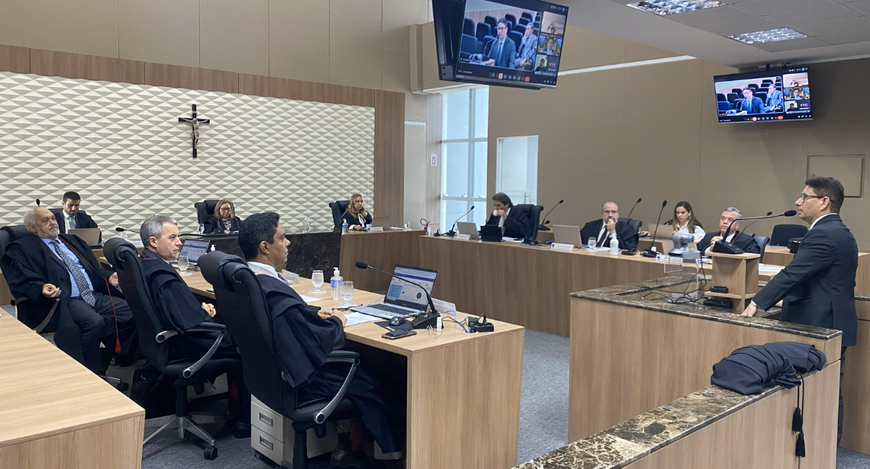 A imagem mostra uma sessão realizada no Pleno do TRE-CE. No centro do espaço há mesas dispostas ...