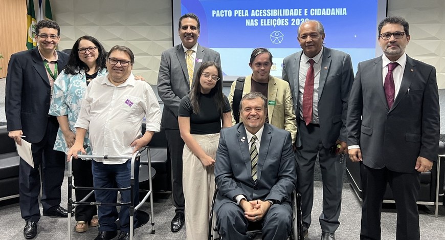 No auditório, um grupo de pessoas posa para foto diante de uma tela de projeção, ao centro, um h...