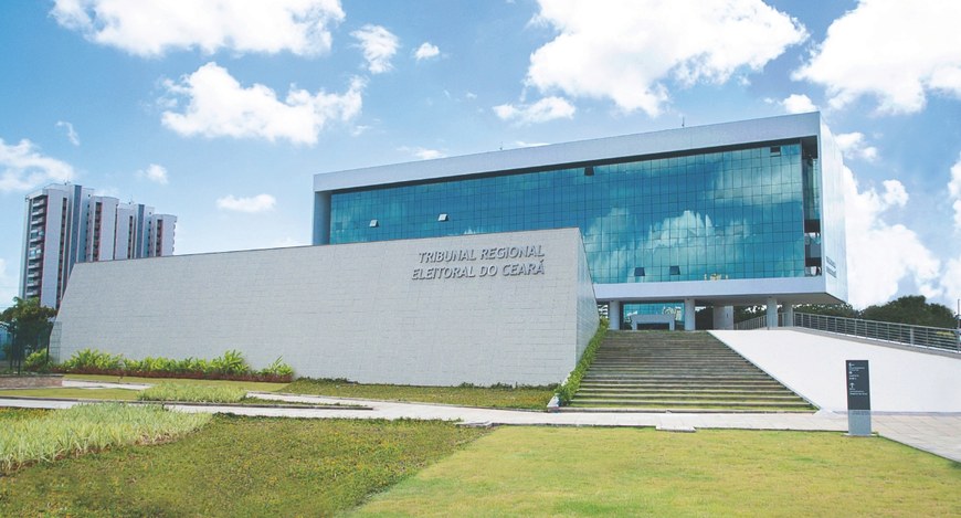 Na imagem, aparece a fachada da sede do TRE-CE, com grama na frente, janelas espelhadas e uma ra...