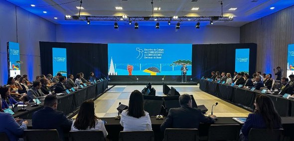 Fotografia de um palco em que há um telão com a logo do 55° encontro do CCORELB, que conta com a...