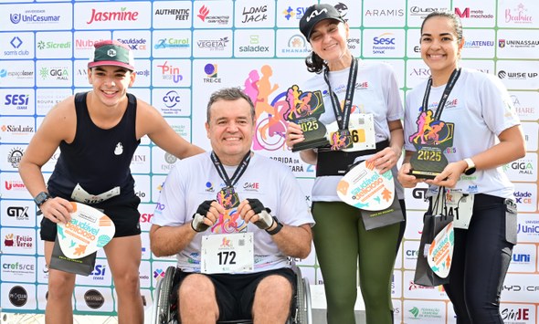 Na quinta imagem, os quatro vencedores da prova posam para foto em frente a um painel com logoma...