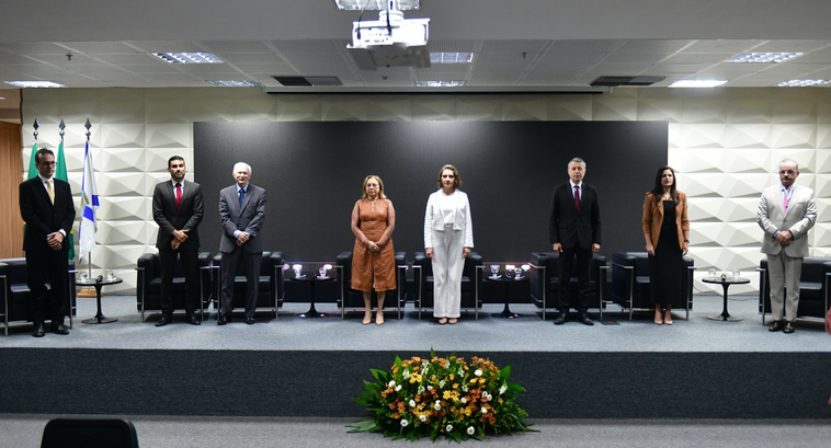 Fotografia de cinco pessoas em pé, lado a lado, em um palco. As três pessoas à esquerda e a pess...