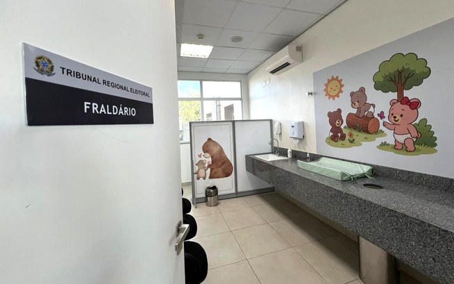 TRE-CE disponibiliza fraldário para melhor receber eleitoras e eleitores na sede, em Fortaleza As imagens mostram o ambiente em dois ângulos diferentes. Na primeira imagem, a porta está parci...