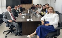 Na primeira imagem, um grupo de pessoas está sentado ao redor de uma mesa retangular, na sala da...