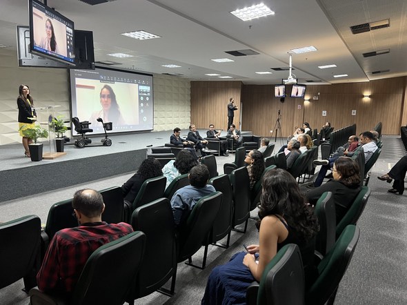 Na primeira foto, no auditório, um grupo de pessoas posa para foto diante de uma tela de projeçã...