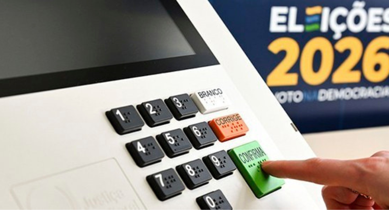 Foto da urna eletrônica em primeiro plano, ao fundo, do lado direito, a logo das eleições 2026