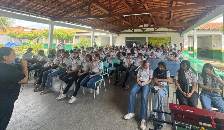Na imagem mostra um espaço coberto em uma escola. No centro do ambiente, há várias fileiras de c...