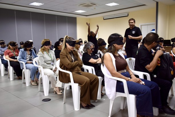 A imagem mostra a sala de treinamento onde ocorreu a atividade. O espaço possui cadeiras brancas...