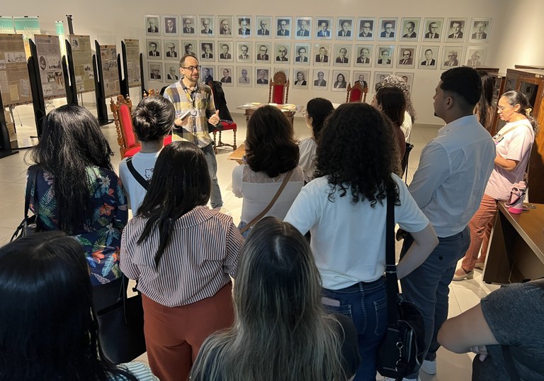 Na imagem, no Centro de Memória do TRE-CE, o mesmo grupo de pessoas está reunido em pé, formando...