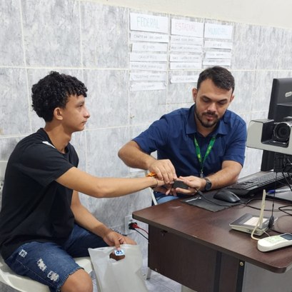 Ação itinerante no distrito de Santa Terezinha totaliza mais de 330 atendimentos eleitorais A imagem é um registro fotográfico quadrangular. Na cena, um servidor está orientando a coleta d...