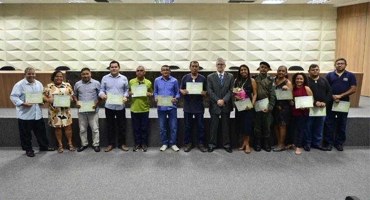 Foto tirada no auditório. Na foto, 13 colaboradores homenageados e e o presidente do Tribunal es...