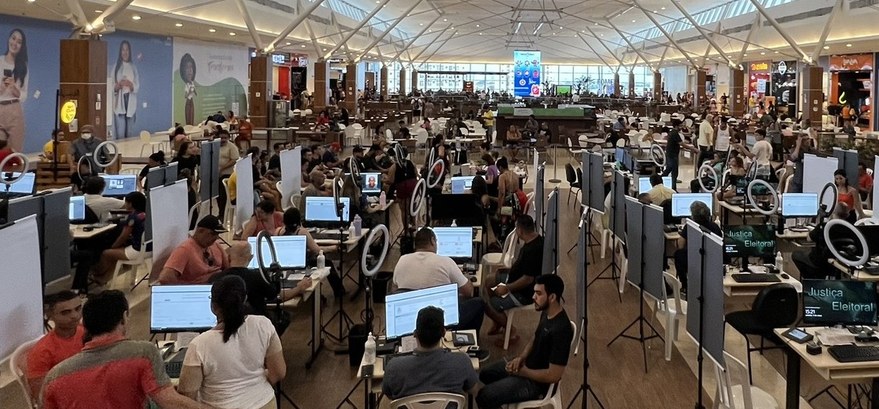 Na foto, em um pátio de shopping, há diversas bancadas de atendimentos do TRE-CE espalhadas pelo...