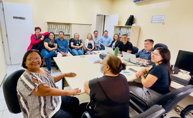 Corregedoria do TRE-CE conclui semana de visitas técnicas em zonas eleitorais da Região Norte do Estado Quinze pessoas estão reunidas em uma sala de escritório, dispostas ao redor de uma grande mesa r...