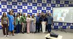 Na imagem, um grupo de 16 pessoas está posicionado em frente a um painel de fundo formado por qu...