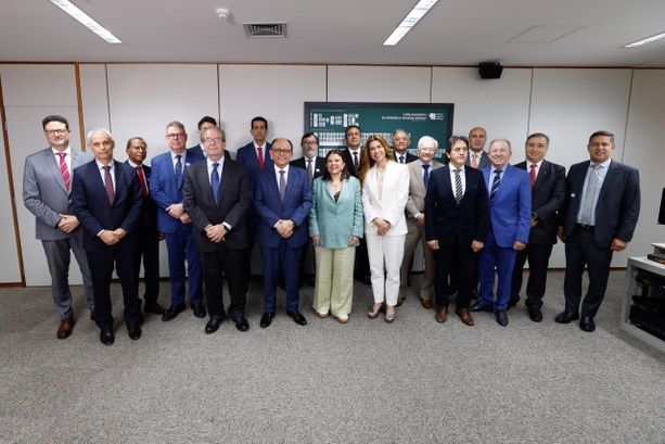 A imagem exibe um grupo pessoas reunidas em pé, alinhadas lado a lado em duas fileiras dentro de...