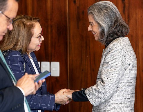 Desembargadora Maria Iraneide participa de reunião no TSE sobre as Eleições 2026 As presidentes do TSE e do TRE-CE estão em pé, diante de uma parede de madeira, cumprimentando-s...