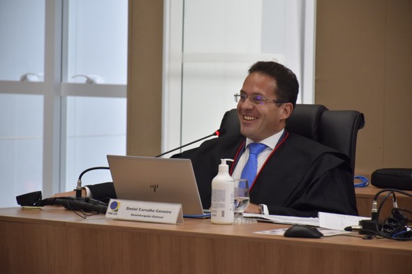 A imagem mostra o desembargador Daniel Carneiro sentado em sua cadeira no Pleno. Sobre a bancada...