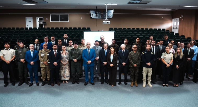 Na imagem, mostra um grupo de pessoas reunido no auditório, posicionadas em duas fileiras de fre...