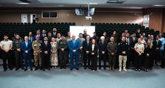 Na imagem, mostra um grupo de pessoas reunido no auditório, posicionadas em duas fileiras de fre...