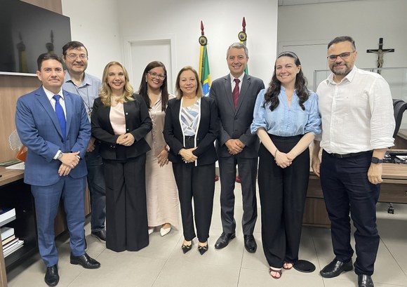 Na imagem, aparecem oito pessoas — quatro mulheres e quatro homens — posando para a foto. Entre ...