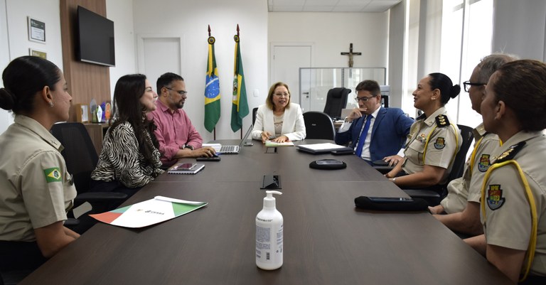Homenagem: curso da Casa Militar recebe nome da presidente do TRE-CE Na imagem, oito pessoas estão reunidas sentadas ao redor de uma mesa retangular. Sobre a mesa, h...