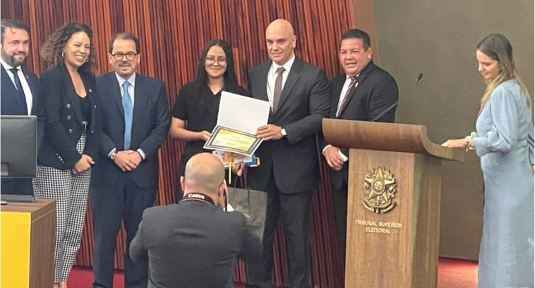 Jovem cearense é premiada no TSE por redação sobre voto e democracia A imagem é um registro fotográfico. Nele, estão sete pessoas posando para uma outra foto, sobre ...