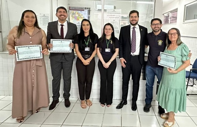 A foto mostra sete pessoas em pé, lado a lado, entre os representantes da Zona Eleitoral e três ...