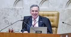 A imagem mostra o ministro Luís Roberto Barroso sorrindo. Ele veste toga preta e está sentado em...
