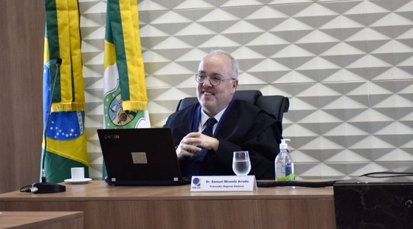 Na sessão do TRE-CE, palavras de reconhecimento marcam despedida do titular da Procuradoria Regional Eleitoral A imagem mostra Samuel Miranda sentado atrás de uma bancada de madeira. Sobre a bancada, há um n...