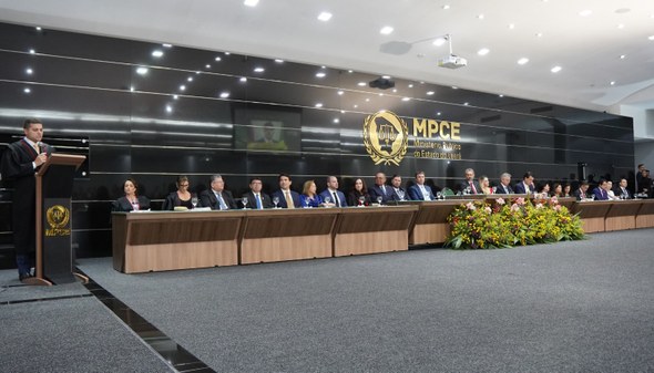 Na imagem, no auditório do MPCE, à esquerda, o empossado está em pé, no púlpito, segurando um mi...