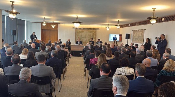 As três imagens mostram o evento. Na primeira, há uma sala com várias pessoas sentadas em cadeir...