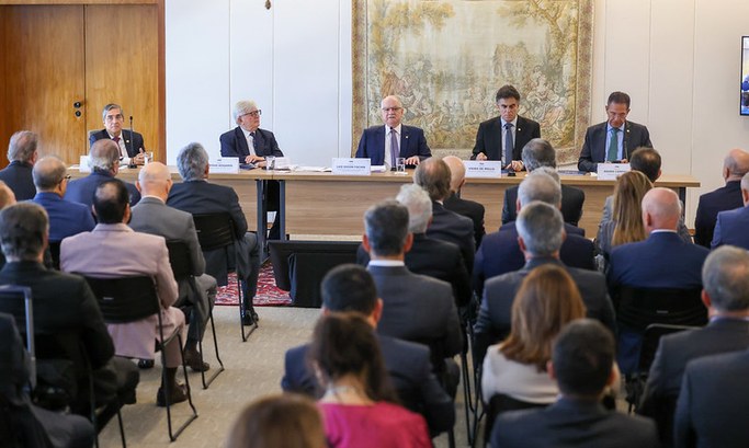 As três imagens mostram o evento. Na primeira, há uma sala com várias pessoas sentadas em cadeir...