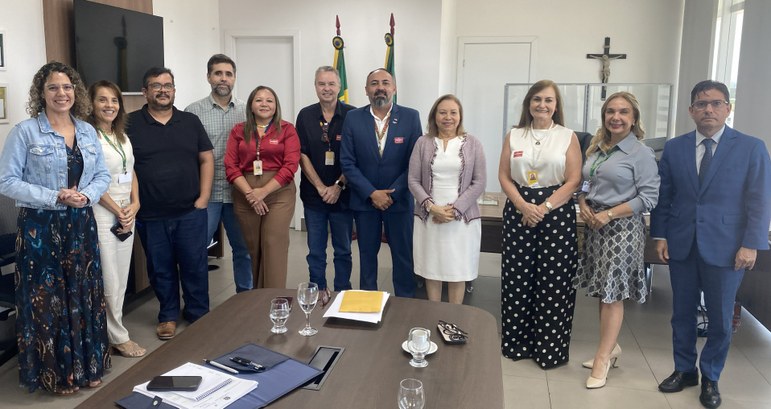 A segunda imagem, na mesma sala, as pessoas estão sentadas ao redor de uma mesa retangular duran...