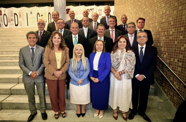 A imagem mostra um grupo de pessoas posando para fotografia em uma escadaria, entre elas, está a...