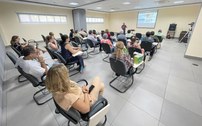 O registro mostra, em plano amplo, os participantes da palestra sentados e voltados para o pales...
