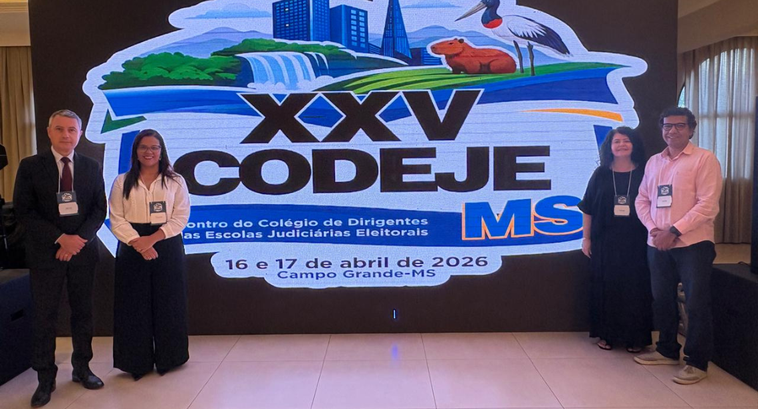 Na imagem, quatro representantes do TRE-CE estão posicionados diante de um painel eletrônico com...