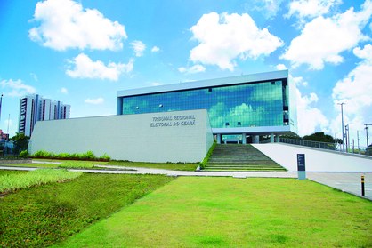 Na imagem, aparece a fachada da sede do TRE-CE, com grama na frente, janelas espelhadas e uma ra...