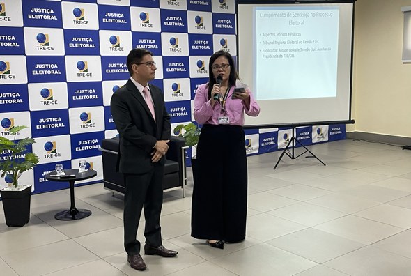 Na imagem, o juiz aparece ao lado da servidora Roberta Laena. Ambos estão posicionados ao centro...