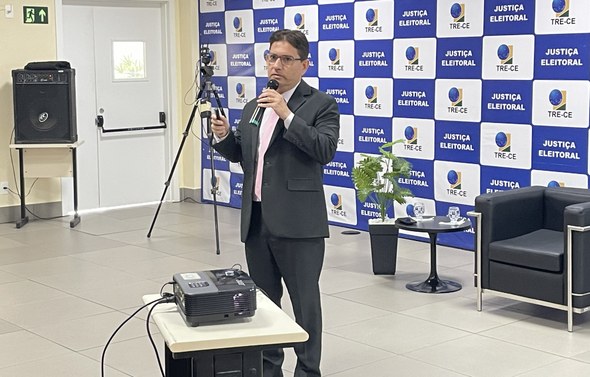 Na imagem, o juiz Alisson Simeão está com um microfone enquanto fala aos participantes. À sua fr...