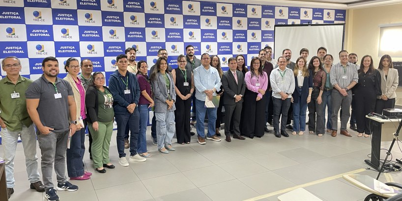 A  imagem mostra um grupo de pessoas, entre homens e mulheres, posando lado a lado para a foto. ...