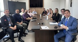 Na primeira imagem, um grupo de 13 pessoas está reunido em uma sala de reuniões, ao redor de uma...