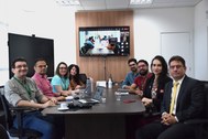 Na primeira imagem, oito pessoas estão sentadas ao redor de uma mesa de reuniões, sendo cinco de...