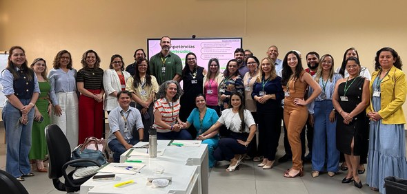 Na imagem, cerca de trinta pessoas posam para uma foto coletiva. Elas estão organizadas em duas ...