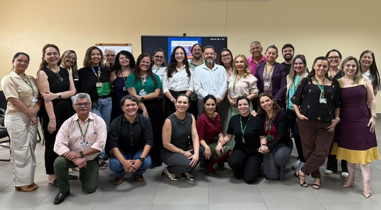 Na imagem, cerca de trinta pessoas posam para uma foto coletiva. Elas estão organizadas em duas ...