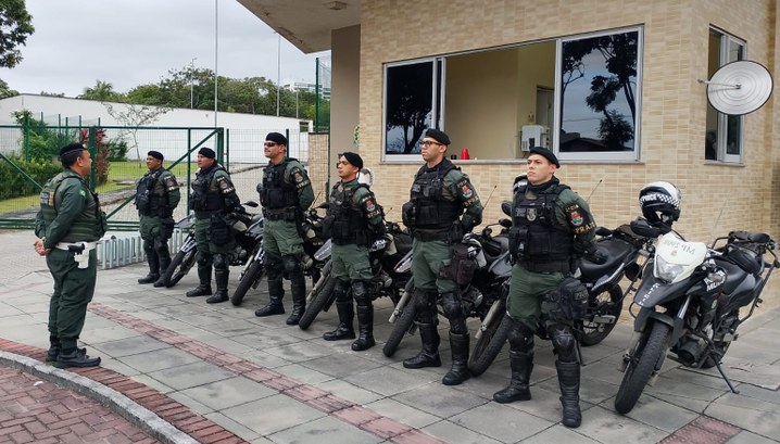 Na primeira imagem, um grupo de sete policiais militares está em formação, em pé, diante do préd...