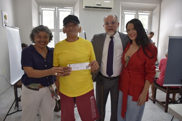 A imagem mostra quatro pessoas - duas mulheres e dois homens - em pé, lado a lado. Um dos homens...